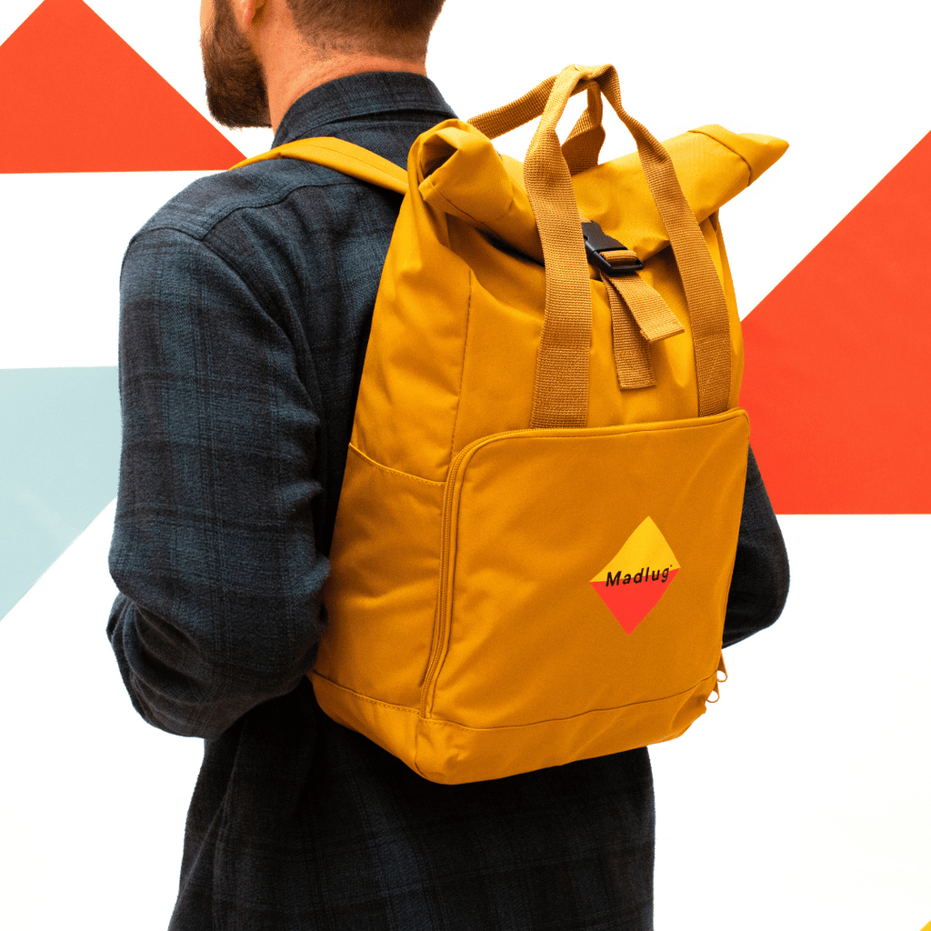 Madlug Roll-Top Backpack in Mustard. Modelled holding rear profile.