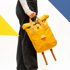 Madlug Roll-Top Backpack in Mustard. Modelled holding bag side profile.