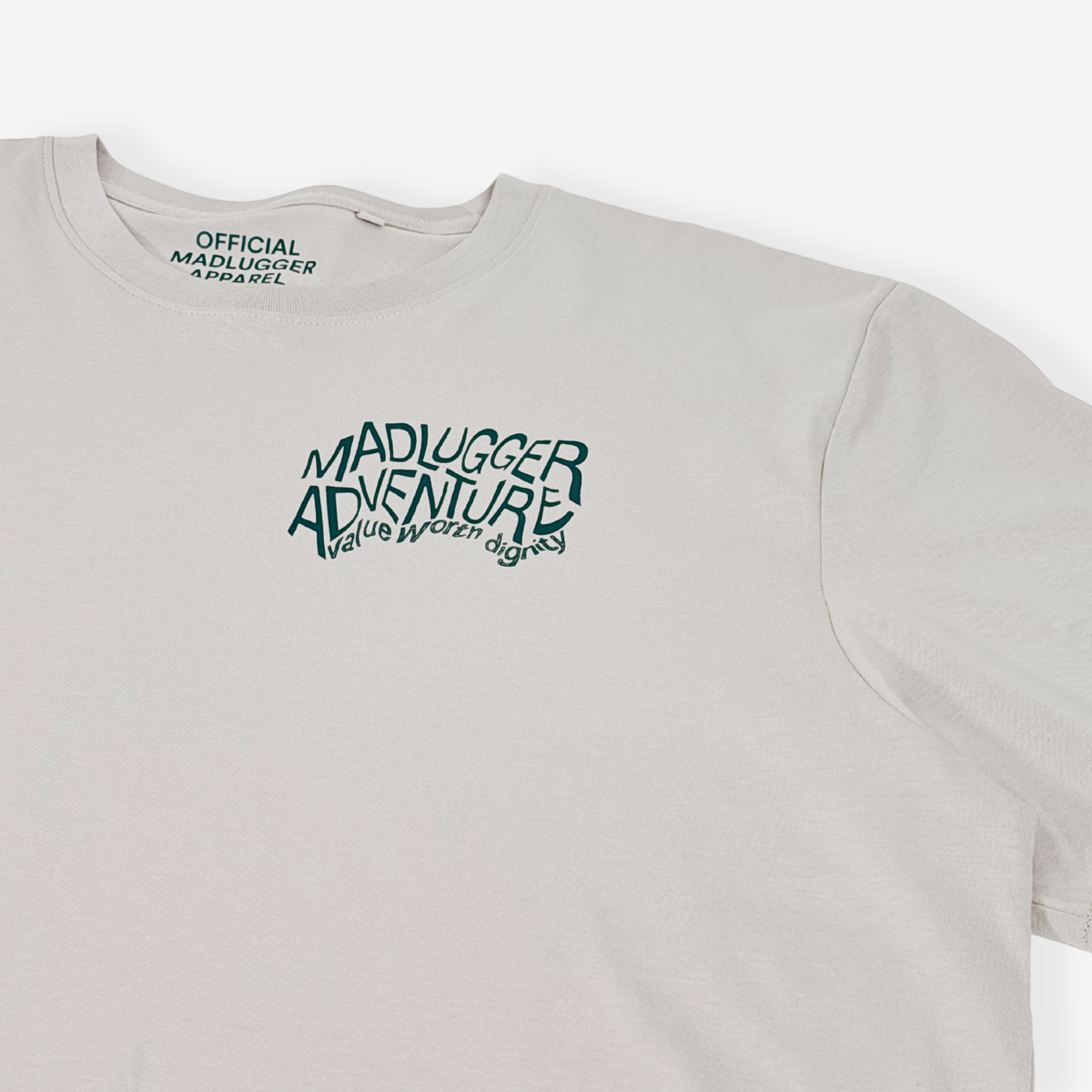A pine green crewneck t-shirt with a stylised white graphic on the chest reading 'MADLUGGER ADVENTURE and 'OFFICIAL MADLUGGER APPAREL' printed inside the collar, shown against a light gray background.